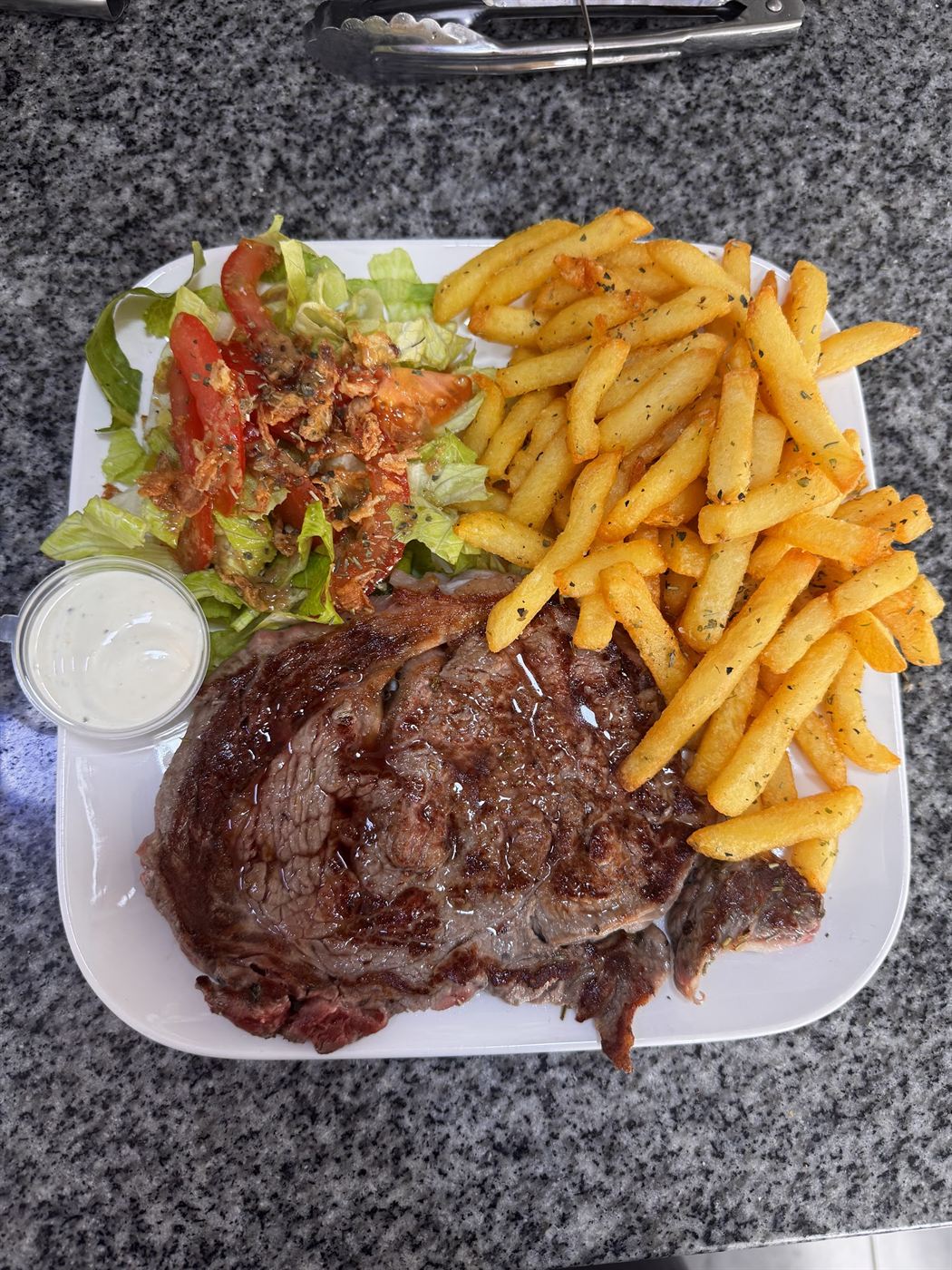 Assiette de viande grillée avec frites épicées, salade et sauce