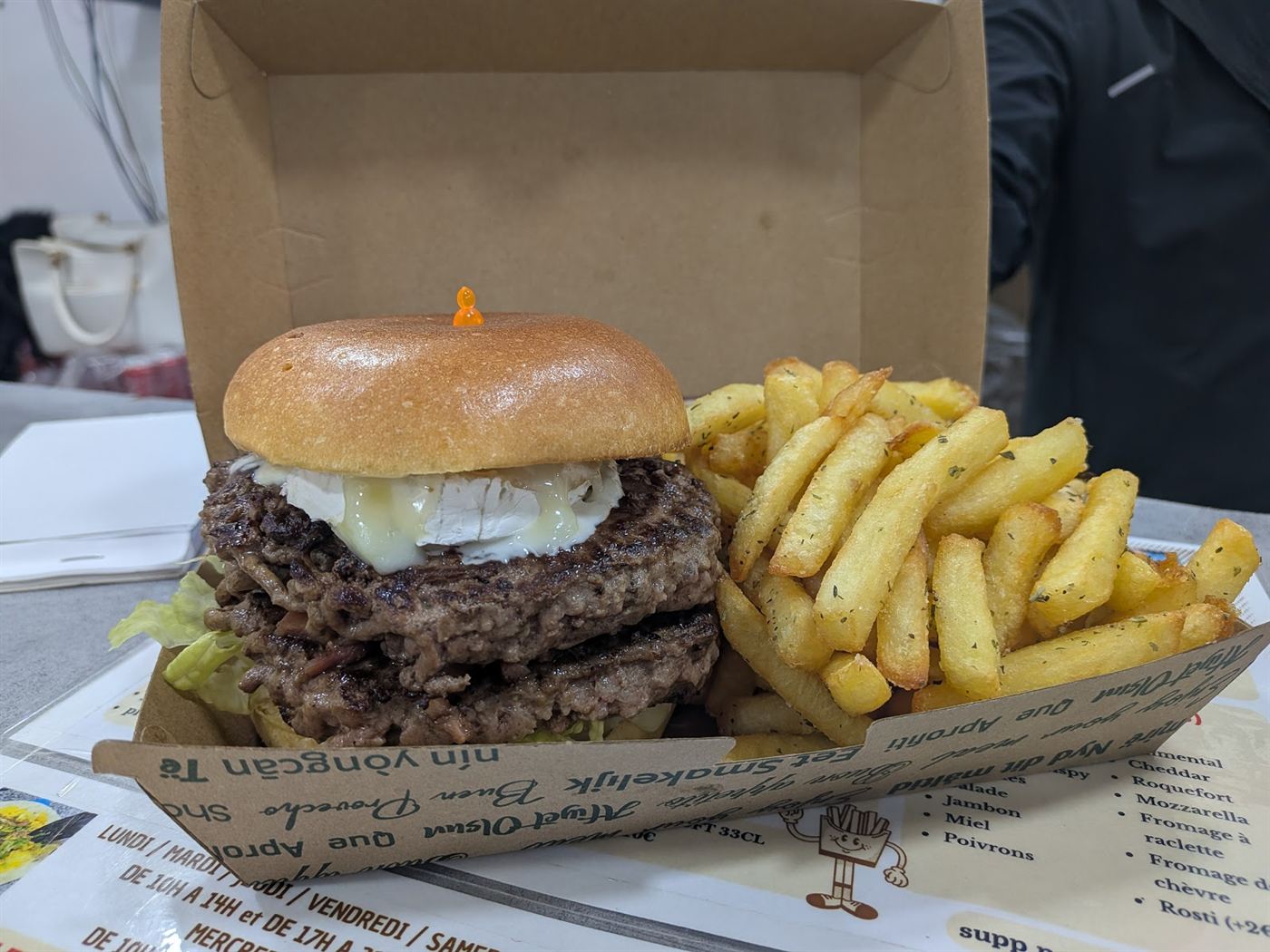 Burger double steak servi avec des frites épicées dans une barquette en carton